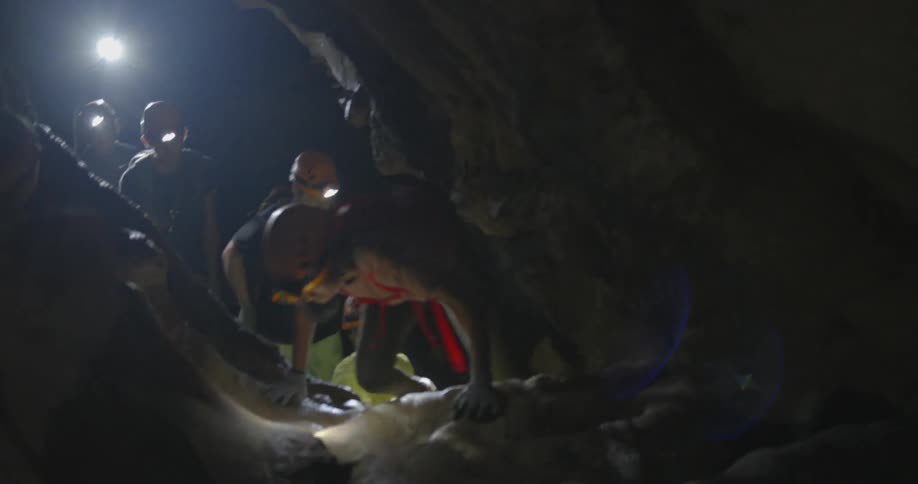 People wearing headlamps crawl through a cave