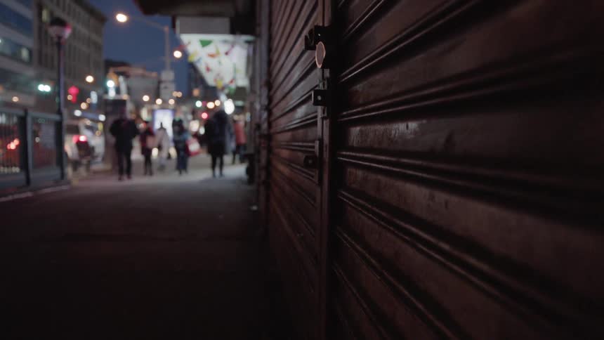 Pedestrians walk on a city sidewalk at night