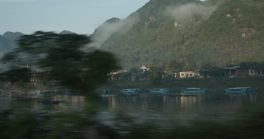 Clouds are clinging to the mountains surrounding a village on a sunny day
