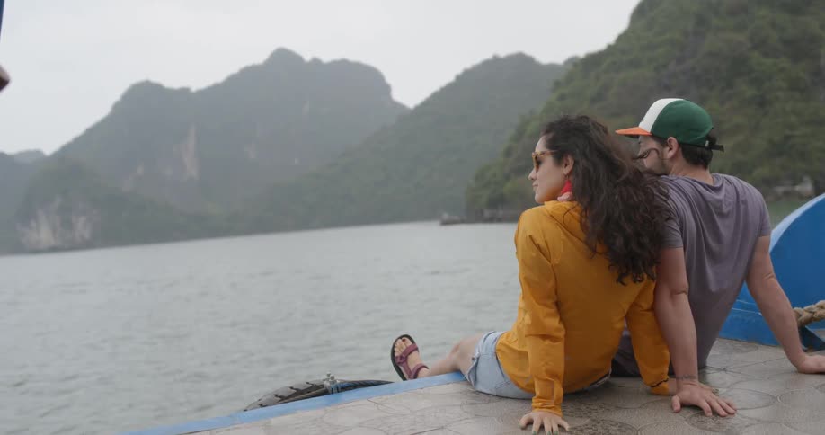 Two people sit on a moving boat looking at the view