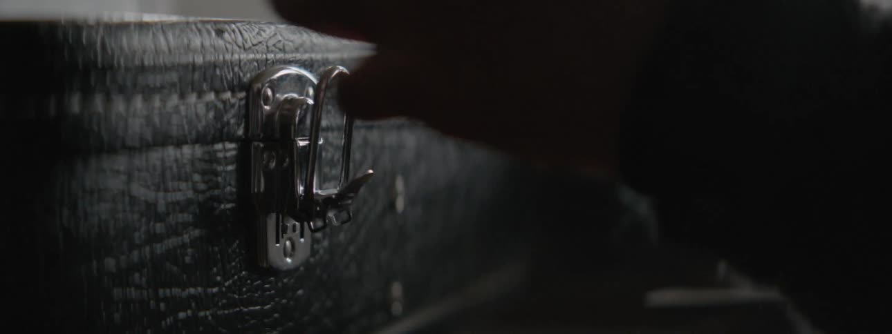A hand unlatches a guitar case