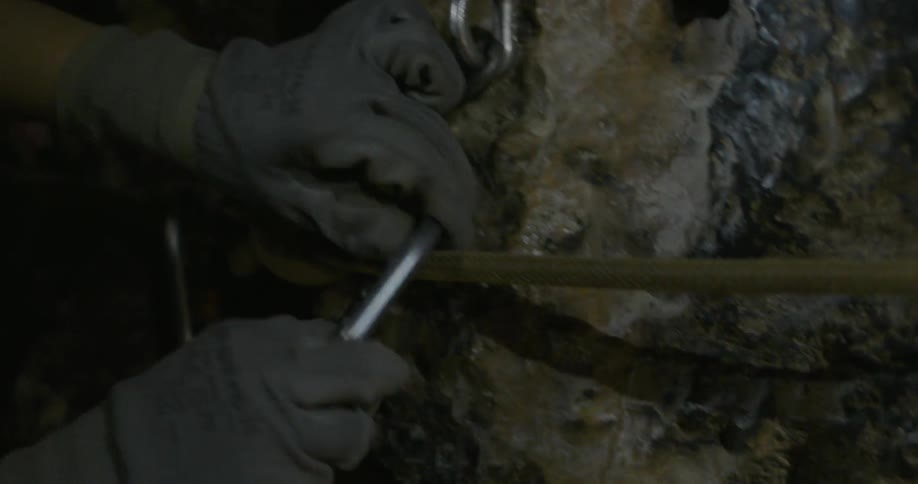 A woman is securing a line to a wall in a cave using carabiners
