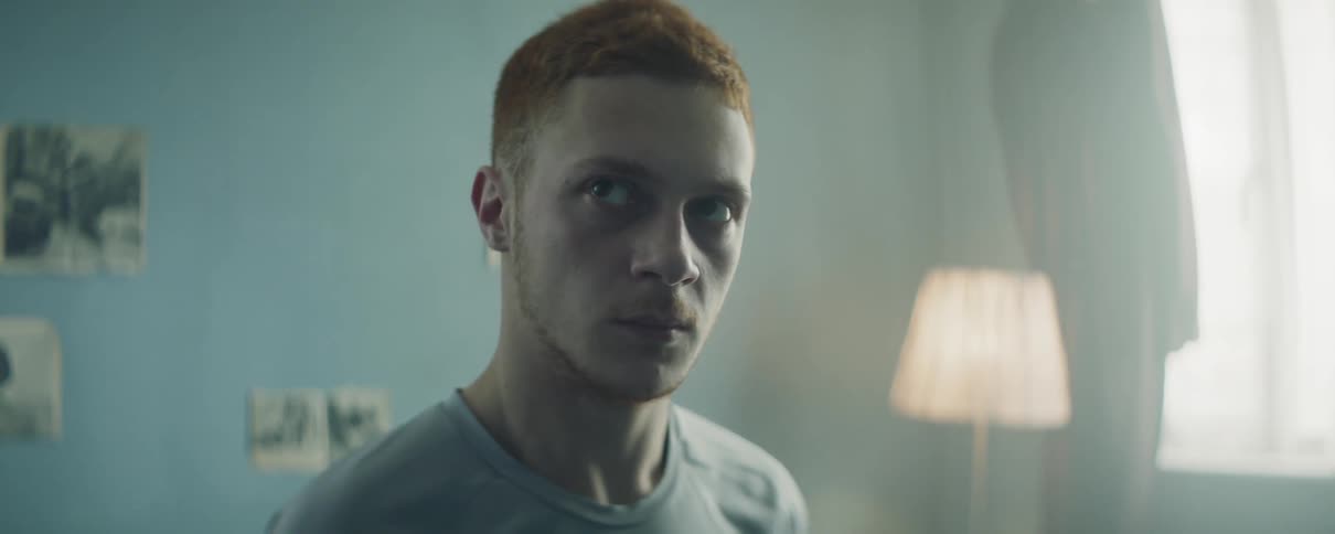 A redheaded man stands in a bedroom