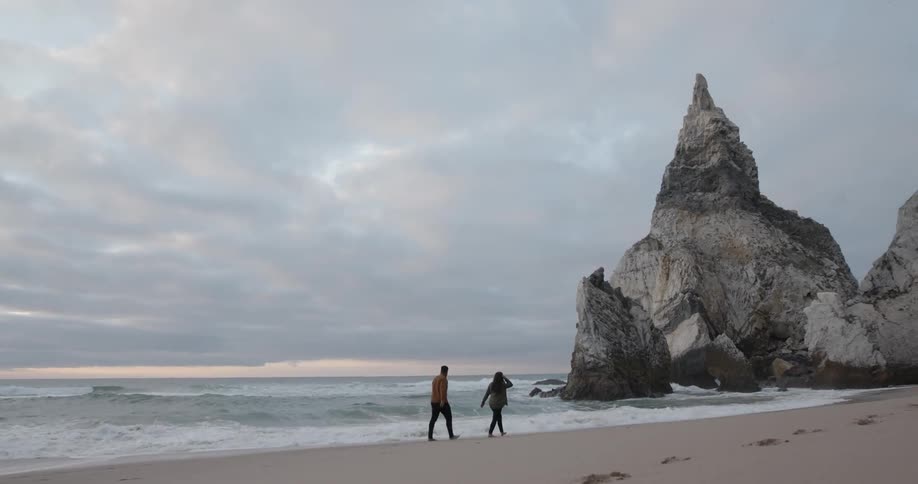 Man and woman walking on ocean beach on cloudy day