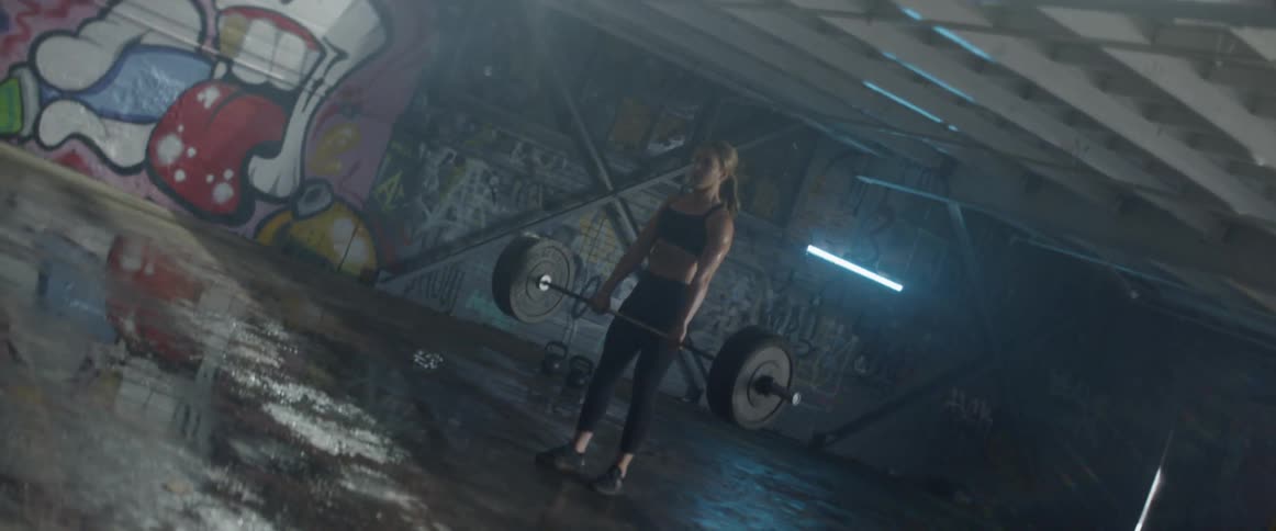 Woman does deadlifts with a large barbell in a warehouse