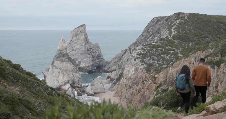 Two people walk over the mountain by the shore