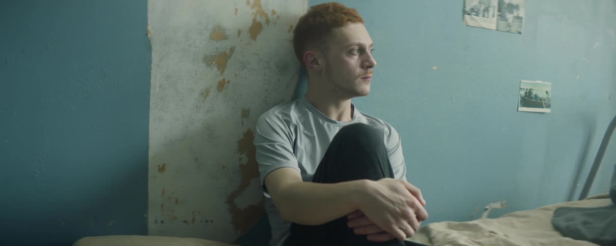 A man sits on a bed leaning against the wall