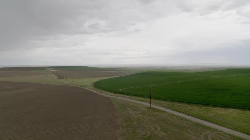 Ascending from a plowed field to reveal lush green cropland under storm clouds