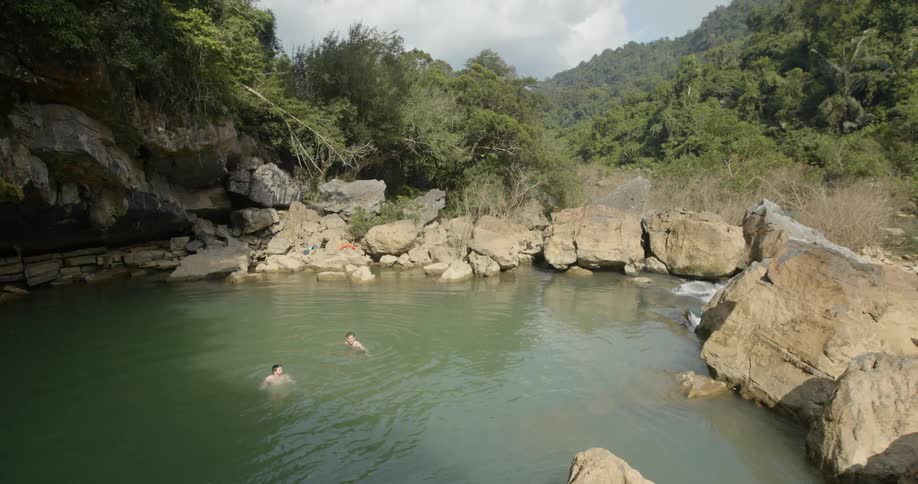 Two people are swimming in forest water hole in cloudy day