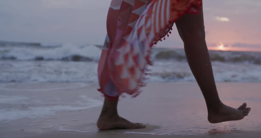Woman is walking on windy ocean beach at sunset