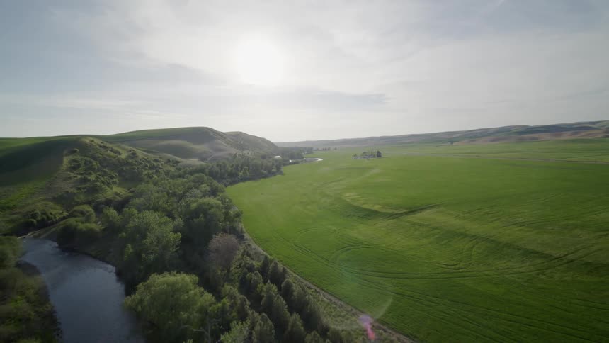 Beautiful green farm fields run along a sparkling river and contoured foothills
