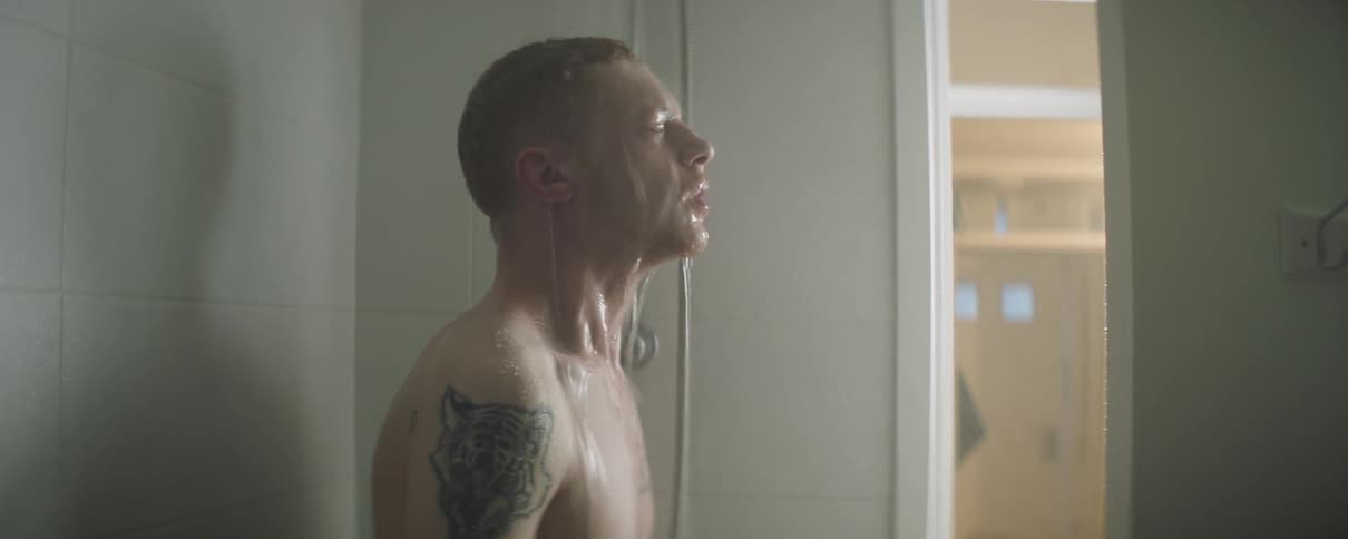 Man with a tattoo on his arm stands in the shower