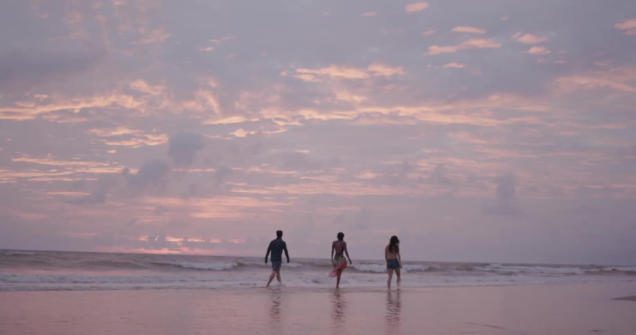 Three people walk on the beach at sunset