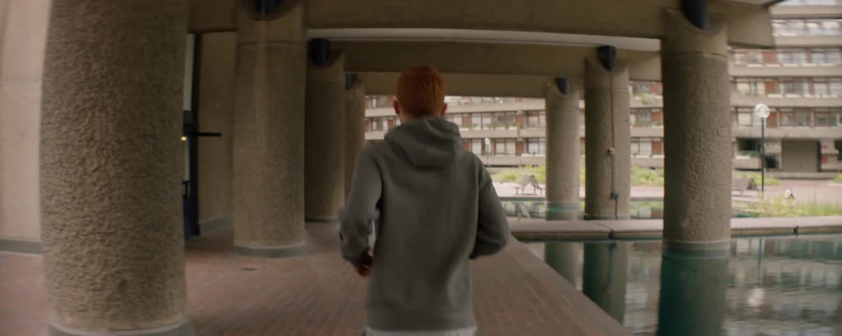 Man in a hooded sweatshirt jogs near the pillars of a building