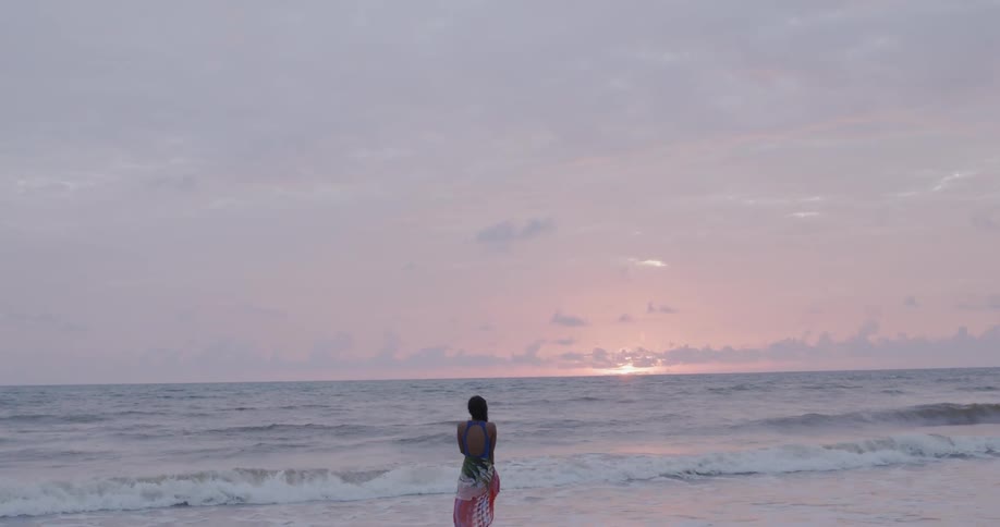 Woman stands on a beach at sunset