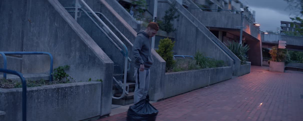 A redheaded man carries and drops a trash bag