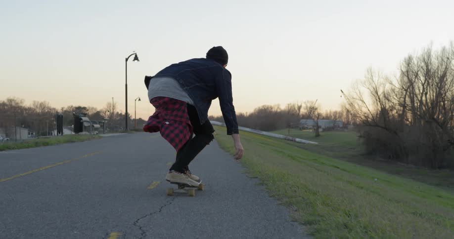 Man skateboards down a country road at sunset