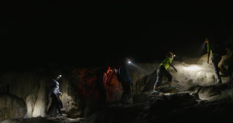 People wearing headlamps walk through a rocky cave
