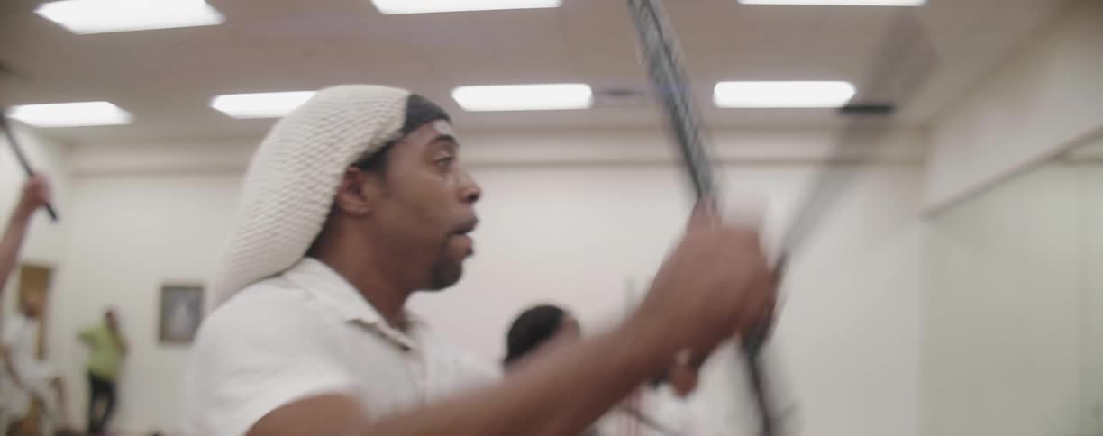 A group of people are practicing a rhythm routine inside in daylight
