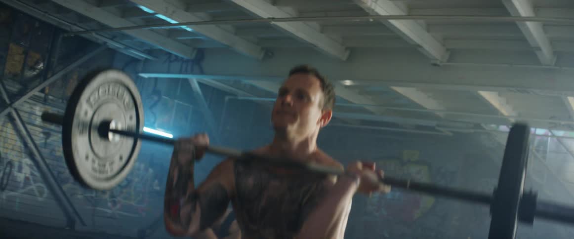 Man and woman lift weights in a building with graffiti