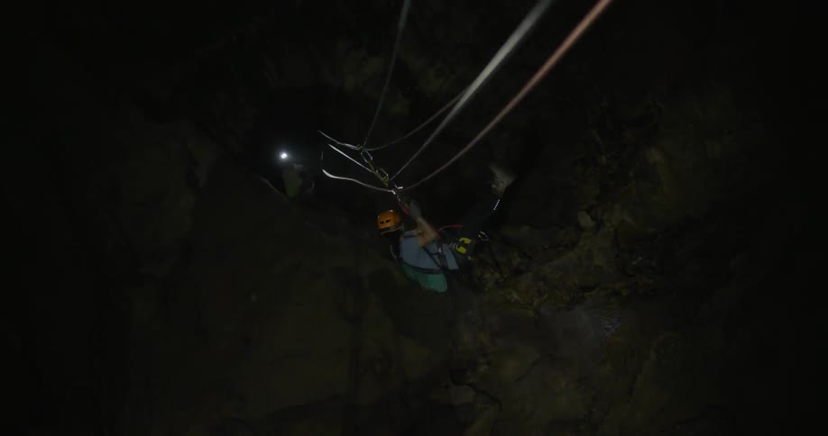 Woman wearing a headlamp is spelunking into a cave