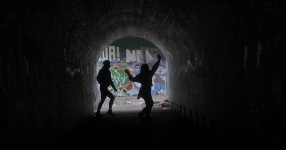 Two women dance in a dark tunnel