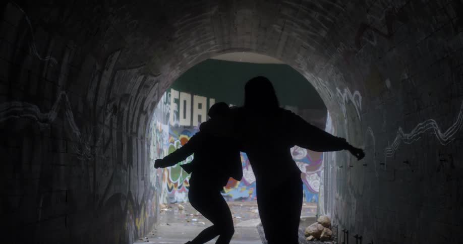 Two women dance in a dark tunnel