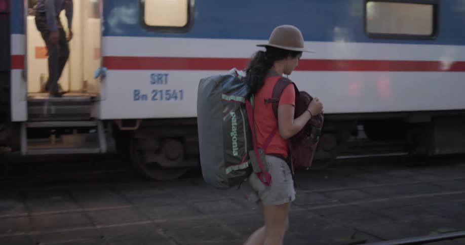 A woman is carrying a backpack as she walks outside a train station at dusk