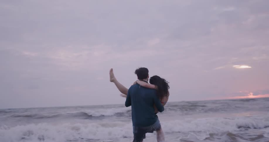 A man and woman embrace playfully on the beach