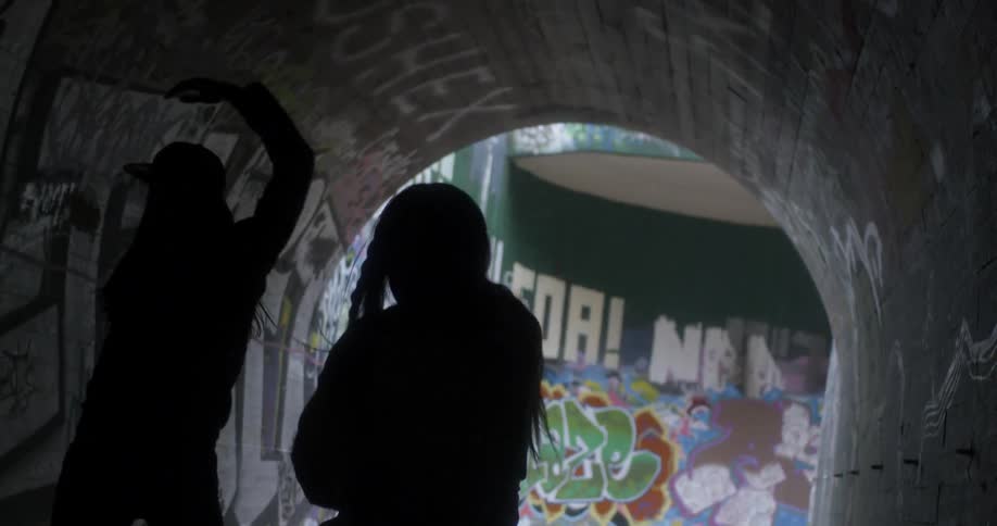 Two young women dance in a tunnel