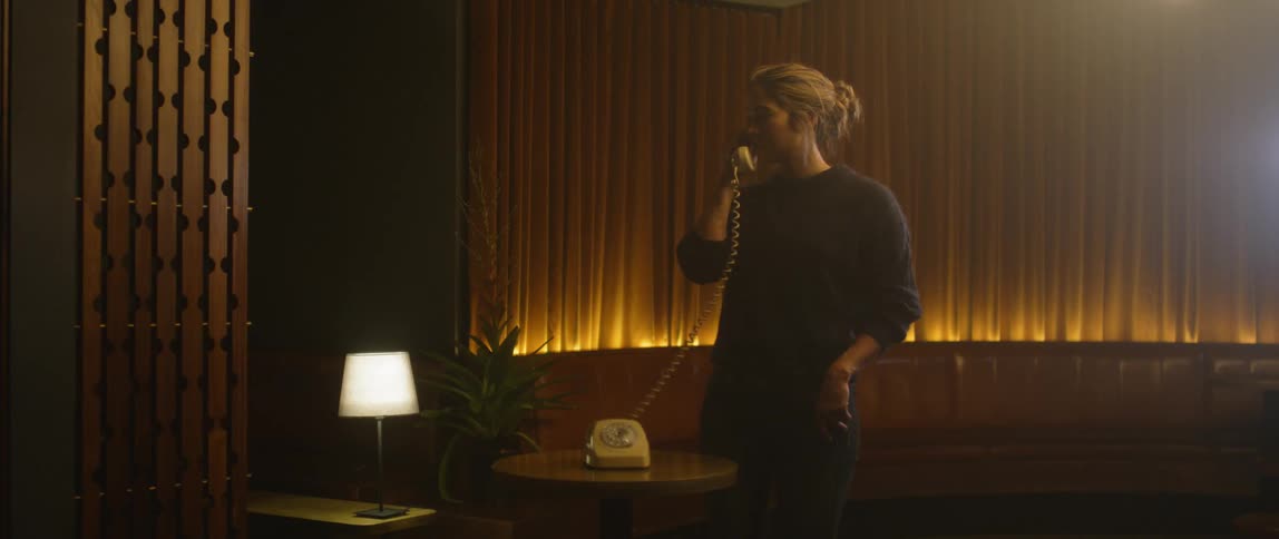 A woman is looking around a room as she talks on a telephone at night