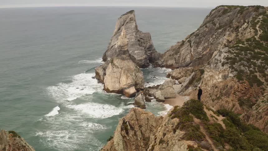 Man standing on huge rock cliff overlooking ocean