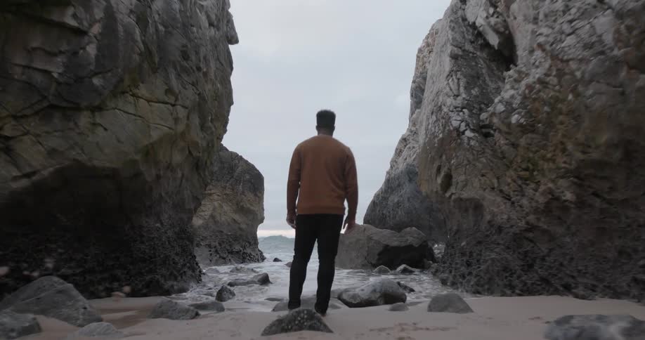 Man stands on a beach near large rocks