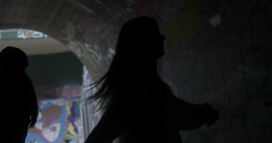 Women dance in a tunnel covered in graffiti