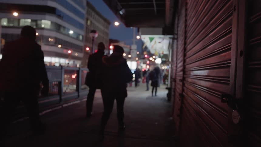 A group of people walk down the sidewalk in a busy city at night