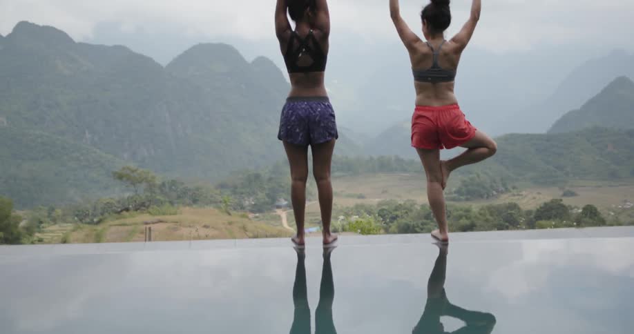 Women do yoga on the edge of a pool in mountains