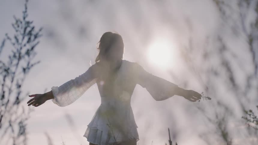 Woman in a white outfit stands with her arms outstretched