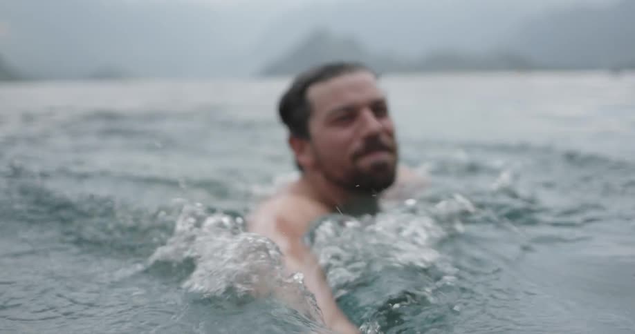 Man is smiling and swimming in cold lake on cloudy day
