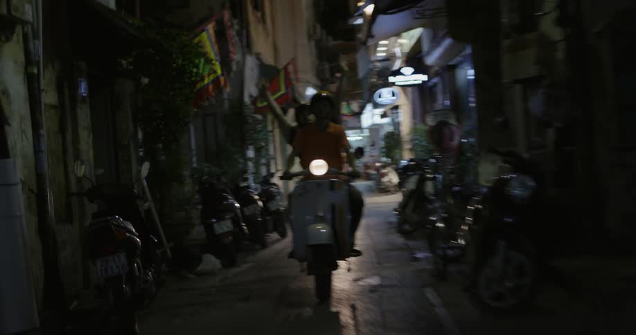 Boys ride on scooter through narrow urban street