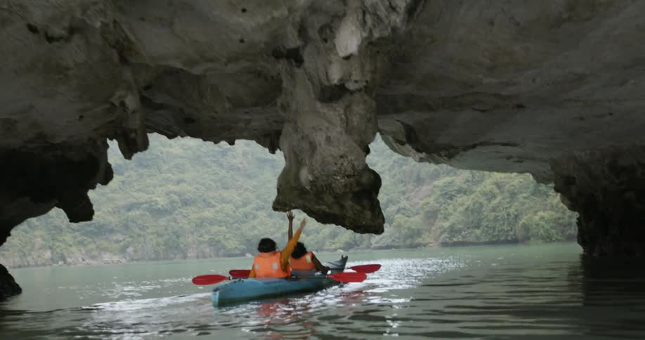 Women kayak beneath a rock formation