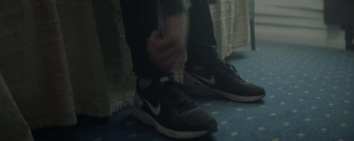 Man sitting on bed is leaning forward and adjusting his shoes