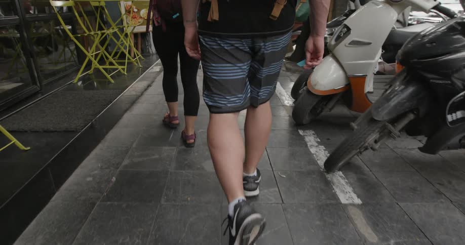 Man with a backpack follows a woman walking down the sidewalk near the market