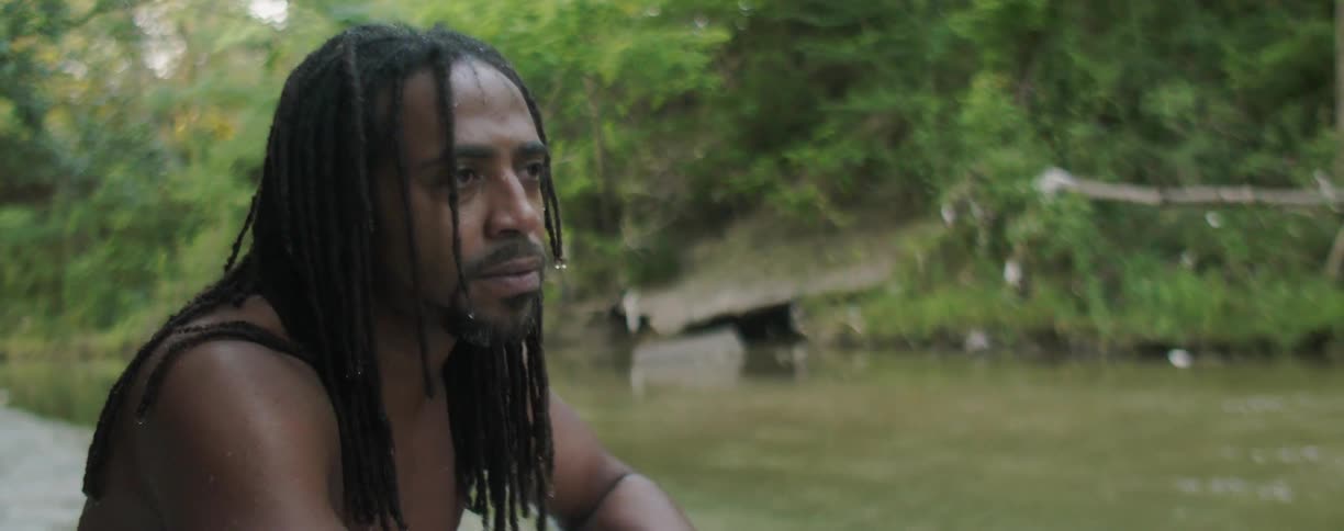 A man is sitting by a riverside and calling his dog in daylight