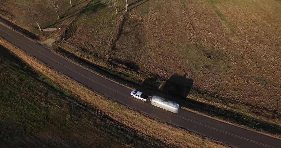 A truck is towing a travel trailer as it drives on a rural road in daylight