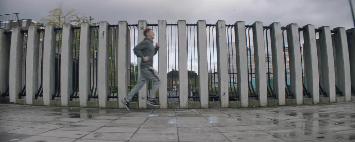 A man runs past the large fence on a cloudy day