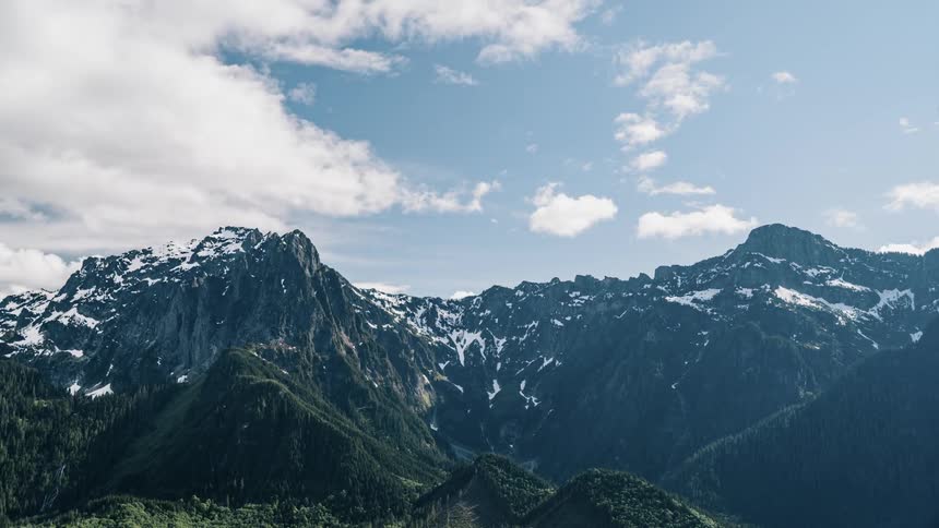 Clouds roll over snowy mountain tops - 4K Time Lapse