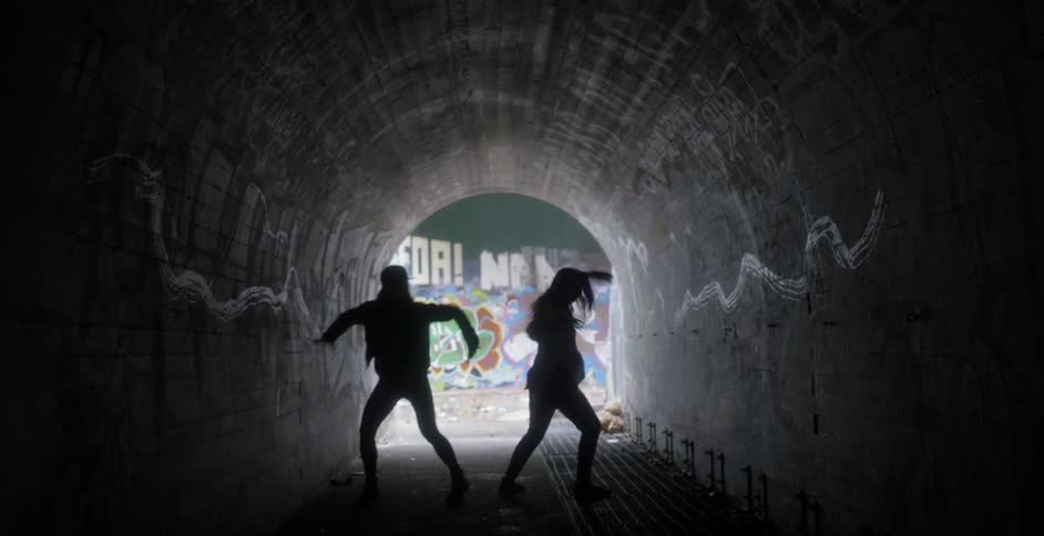 Two women dance in a dark tunnel