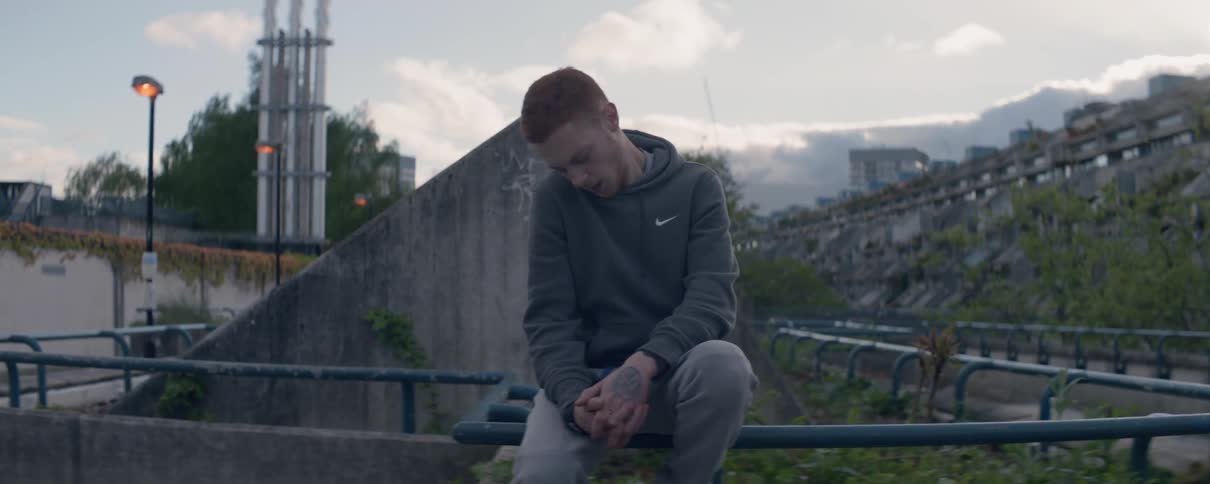 A man is sitting on a fence railing and stretching his neck outside at dawn