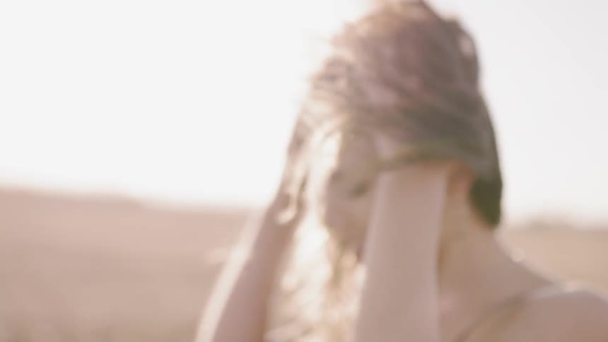 Woman stands in a field as she cries under a sunny sky