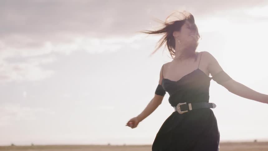 Woman in a black dress runs and spins in a field